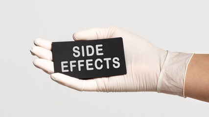 Closeup of the hand in a white sterile glove holding a card with text - Side effects