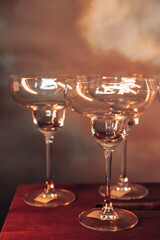 empty martini glasses in a subdued warm light against the background of a wall painted to match the sky around the smoke, party invitation template with free space for text