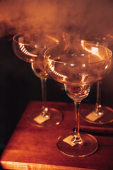 empty martini glasses in a subdued warm light against the background of a wall painted to match the sky around the smoke ,party invitation template with free space for text