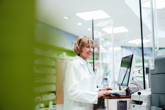 Smiling female pharmacist standing at desk in pharmacy
