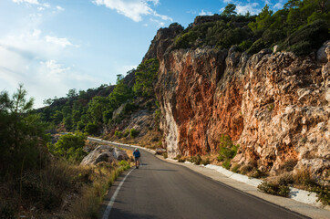 Hiking on Lycian way trail route from Finike to Karaoz. Man is trekking on mountain road with high dramatic cliff, Eco tourism in Turkey