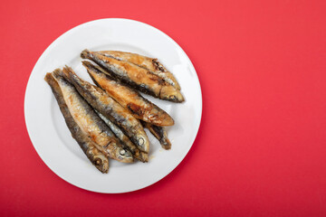 fried small sardines on white plate on red