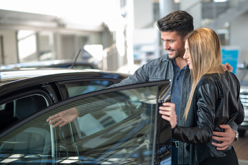 Young couple choosing new car for buying in dealership shop