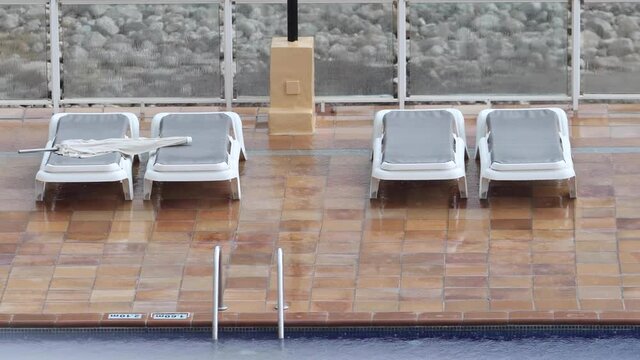 Extremely rainy wether at a holiday resort showing the rain pouring down on empty sun loungers by the side of a hotel swimming pool on the Spanish Island of Ibiza in Spain