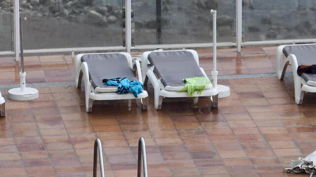 Extremely rainy wether at a holiday resort showing the rain pouring down on empty sun loungers by the side of a hotel swimming pool on the Spanish Island of Ibiza in Spain