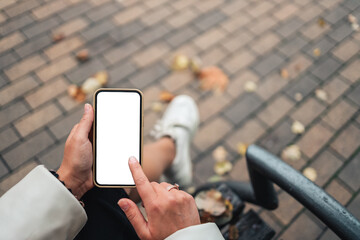 Top view of a woman hands holding smartphone with white blank screen. Copy space in autumn garden. Female reading text and watching video on a mobile phone