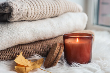 Obraz na płótnie Canvas Burning candle on the windowsill, against the background of warm sweaters and autumn leaves.