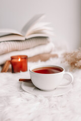 A cup of tea on the window with burning candles and sweaters.