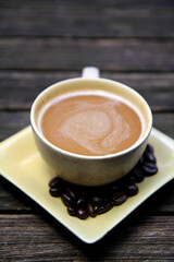 A cup of cappuccino and coffee beans at yellow cup