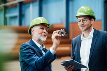 Male professional discussing over equipment with coworker in factory