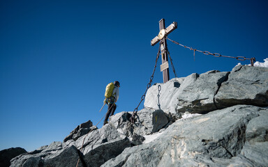 A woman in hiking outfit reaching the cross on Grossglockner, highest mountain in Austria. Clear...