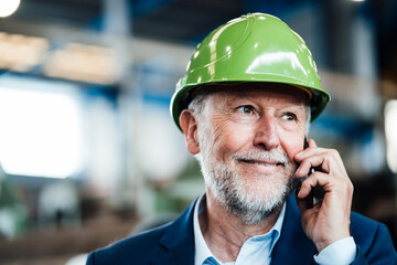 Smiling male manager talking on smart phone in factory