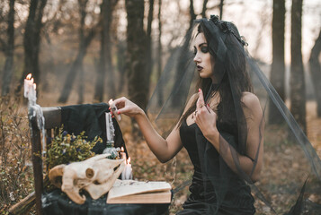 Brunette witch girl conjures in the forest conducts rituals with a fantasy skull nature magic in...