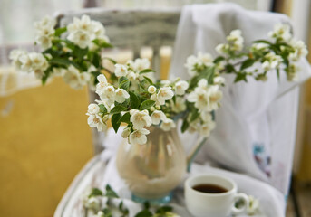 Jasmine flowers in a white vase. Stillife with jasmine and cup of coffee.