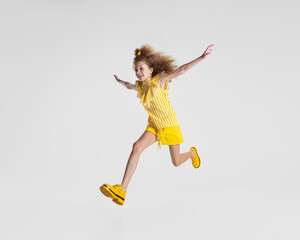 Full-length portrait of little active Caucasian preschool girl in bright yellow outfit and shoes running isolated over white background