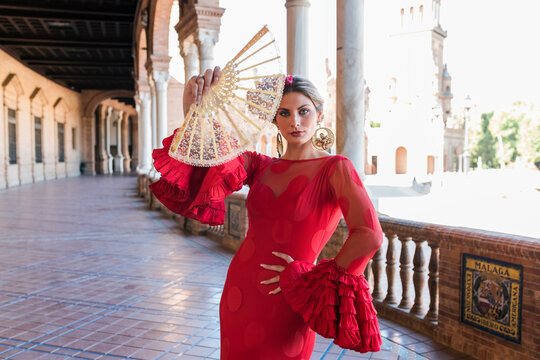 Woman wearing traditional dress holding hand fan at Plaza De Espana walkway in Seville, Spain