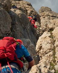 mixed gender group  of climbers in a via ferrata named rodella in the dolomites of south tyrol, italy, with colorful attire, rucksacks and helmets