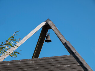 Old and antique cast iron school bell hangs in the ridge of the wooden roof of a school