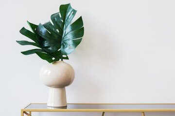 minimalistic image of a vase with monstera leaves against a white wall. Modern interior details. Stylish room decoration. Space for text.