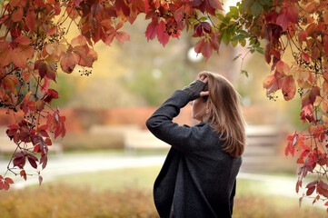 Woman with long blond hair stands in autumnal colored wild grape natural arc