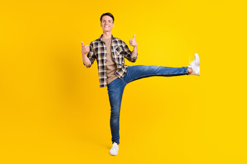 Fototapeta na wymiar Photo of promoter flexible guy raise leg show thumb up wear plaid shirt jeans shoes isolated yellow color background