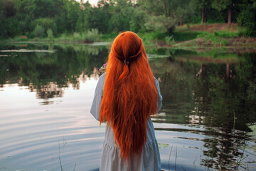 A girl in a blue dress stands in the water of a picturesque lake. Art photo from back no face. Hair...