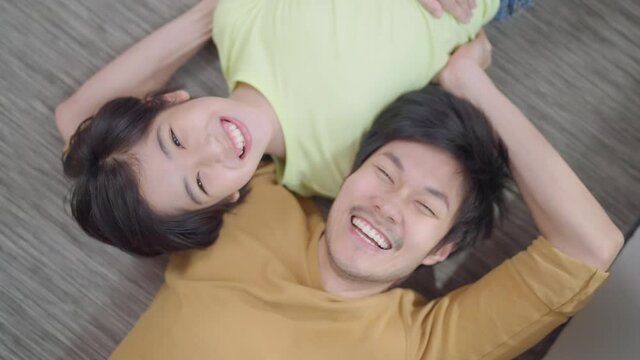 funny family moment asian famuly father lay down with his son playing together laugh smile toothy with cheerful and happiness looking up at camera,pov  dad son sleep on floor look up to camera
