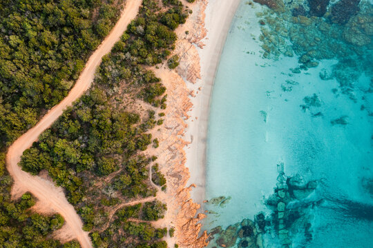 View from above, stunning aerial view of a green and rocky coastline with a white sand beach bathed by a turquoise, crystal clear water. Liscia Ruja, Costa Smeralda, Sardinia, Italy.. © Travel Wild