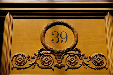 Numéro 39 dans un cercle ouvragé sur façade de bois. Numéro de rue.