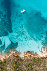 View from above, stunning aerial view of a green and rocky coastline with a sailboat sailing on a turquoise, crystal clear water. Liscia Ruja,Sardinia, Italy..