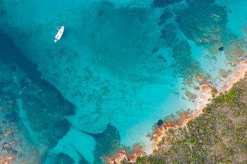 View from above, stunning aerial view of a green and rocky coastline with a sailboat sailing on a turquoise, crystal clear water. Liscia Ruja,Sardinia, Italy..