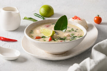 Spicy creamy coconut Tom Kha Gai soup with chicken, cherry tomato, coconut milk, kaffir, galangal, lemongrass,mushrooms on light background. Asian Thai food. Close up.