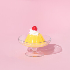 Yellow jelly on dish with cherry on top on pastel pink background. 70s or 80s retro style aesthetic dessert idea. Minimal food concept.