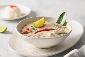 Spicy creamy coconut Tom Kha Gai soup with chicken, cherry tomato, coconut milk, kaffir, galangal, lemongrass,mushrooms on light background. Asian Thai food. Close up.
