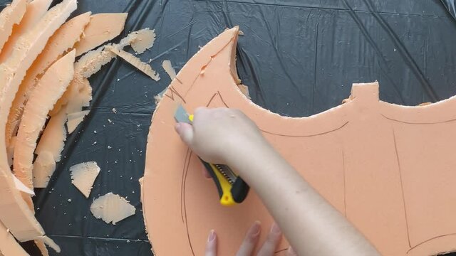 Woman makes viking hatchet for cosplay festival. Hands cut axe form from Styrofoam with stationery knife. Craftsman's workshop. Garbage bag is on table.