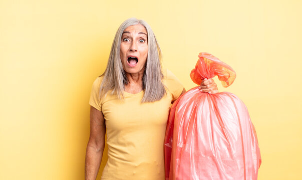middle age pretty woman looking very shocked or surprised. plastic garbaje bag