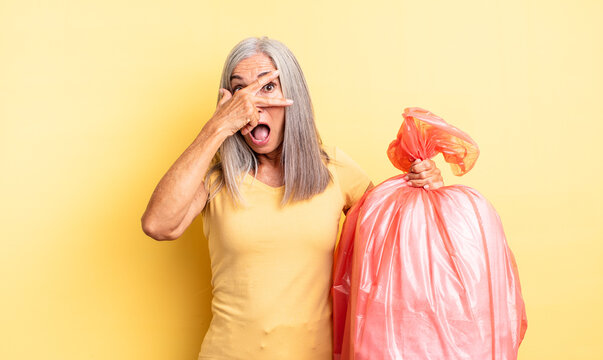 middle age pretty woman looking shocked, scared or terrified, covering face with hand. plastic garbaje bag