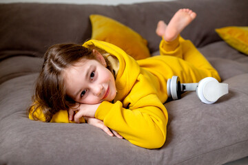 smiling cute little girl in yellow clothes lying in bed with a headphones on listening to the music. High quality photo