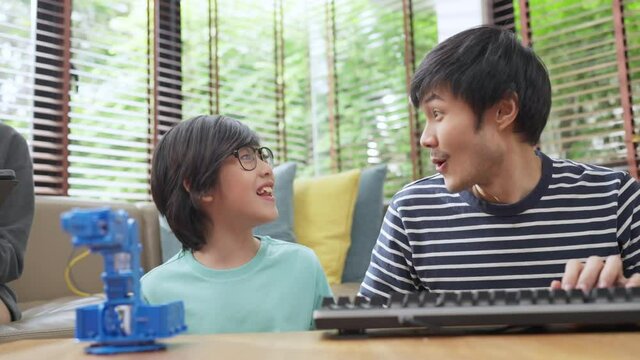 study robot automation at home concept,asian boy child with father mom control robot arm on Digital tablet and computer keyboard, happy family getting a lesson in coding control robotics at home