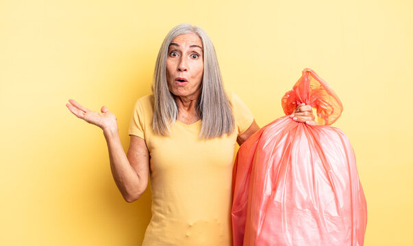 middle age pretty woman looking surprised and shocked, with jaw dropped holding an object. plastic garbaje bag