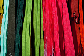 Multicolored zipper locks in a clothing store. Many colored strips of fabric hang on the wall. Clothing accessory close up.