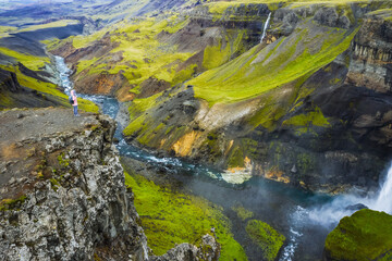 Woman hiker enjoying Highlands of Iceland. River Fossa stream in the Landmannalaugar canyon valley. Hills and cliffs are coverd by green moss