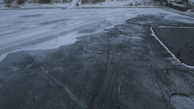 Drone view of a frozen lake with two ice hockey rinks, children train on a winter day
