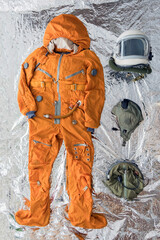 Flat lay of astronaut orange space suit, space helmet and space suit accessories on silver...