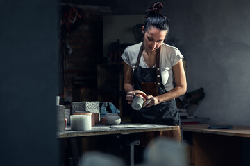 Craftswoman in apron working in her workshop making decorative concrete vase.