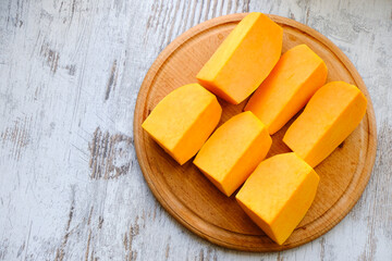 Big pieces and blocks of raw pumpkin in a wooden plate on a light table. Culinary template for pumpkin dishes. Healthy food. Empty space for text or design.