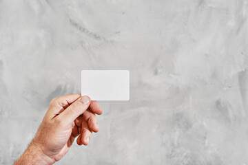 Male hand holding blank white card isolated against neutral gray background. Business card in hand