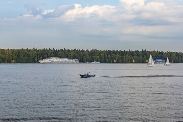 White three-deck ship on a river cruise. The vessel is moored by the green forest