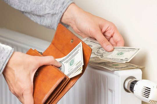 Woman's hand takes US dollars banknotes from wallet and places on heating radiator battery with temperature regulator. Expensive heating costs during cold season. Paying bills