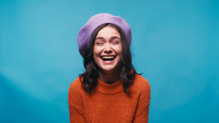 excited woman in warm sweater and beret laughing isolated on blue - obrazy, fototapety, plakaty